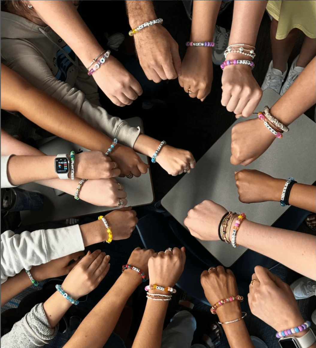 This image features hands coming together in a circle, featuring homemade friendship bracelets