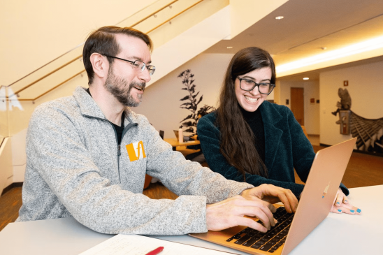 Two students collaborate on a project with a laptop.
