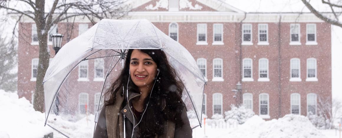 A woman walks with a clear umbrella through a snow-covered campus