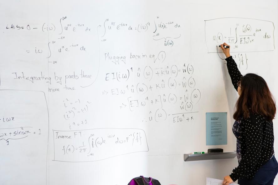 person working on a mathematical equation on a whiteboard
