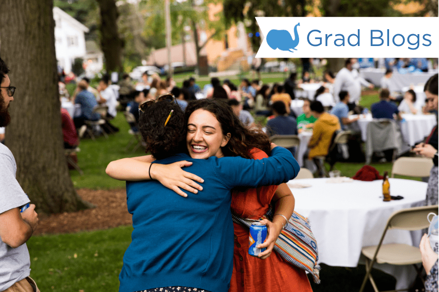 Two students hug at a barbecue with tables and students surrounding them. 