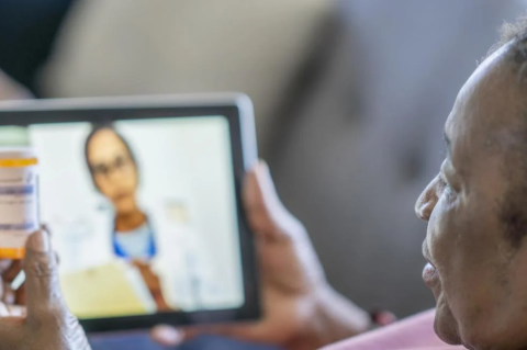 An older woman talking with a doctor on her iPad, while holding up a prescription bottle. A Tufts study of older and chronically ill patients found some upside to remote health-care appointments, but many concerns
