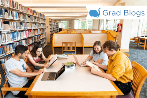 A group of students sit around a table in the Tisch Library, looking at their computers and chatting.