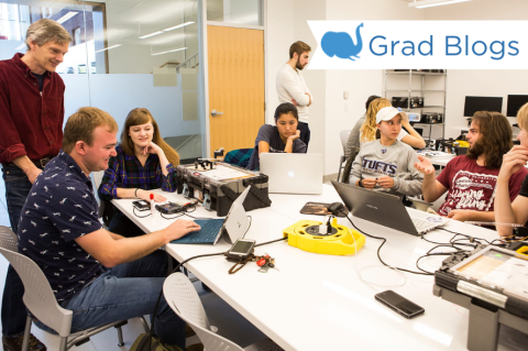 A group of students sit around a table on their laptops working on a project